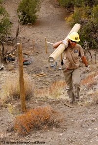Southwest Conservation Corps crew member Zoe carries a post up the steep hill to use as part of an H-brace along Spring Creek Basin's southeastern fence line.